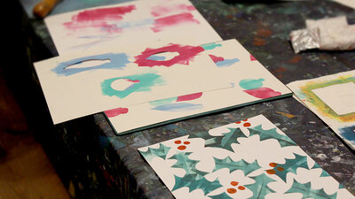 Finished Christmas Card decorated with holly displayed on the table with stencils and other tools used for print making