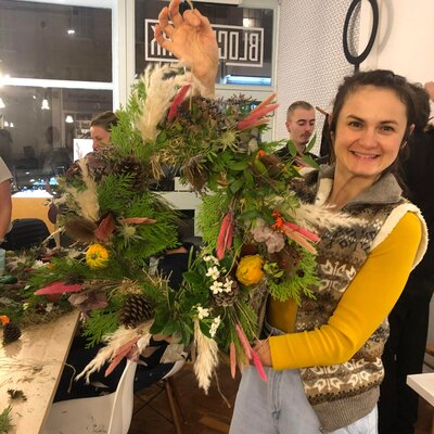 Person poses with autumn wreath decorated with dried flowers and pine cones