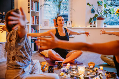Women sit in circle with their arms spread, candles light the room