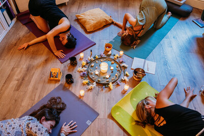 Women in the circle on yoga matts in the pose thread the needle with lit candles, crystals and flowers in the middle.