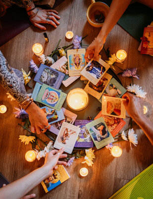 Hands hold Oracle Cards with candles and flowers around them