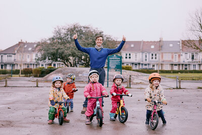 Group of toddlers learning how to balance on bikes all pose for a photo with their instructor