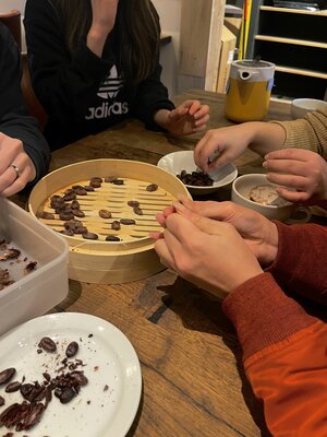 Group of guests sit around table and peel roasted cacao beans 