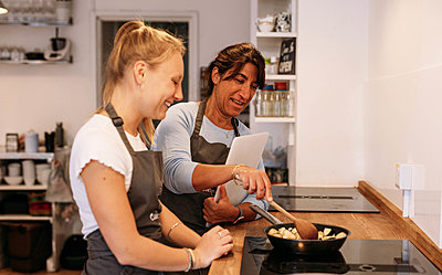 Guest laughs as host reaches over to help stir vegetables in the frying pan