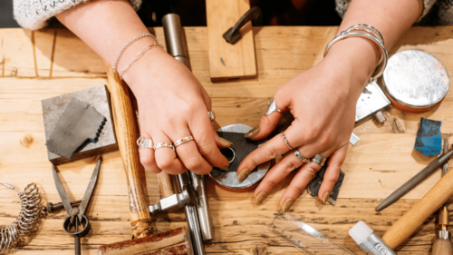a pair of hands craft a silver ring on a table surrounded my jewellery making tools