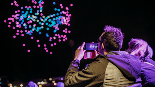 A man holds his phone up to record the drone light performance in the sky