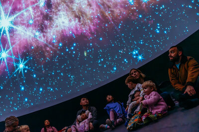 Families gazing at a dazzling starscape in a cosy planetarium.