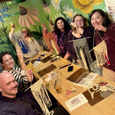 Joyful group crafting macramé in a vibrant, floral-themed room.