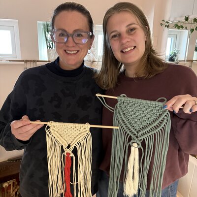 Two smiling women showcasing their handmade macramé creations.