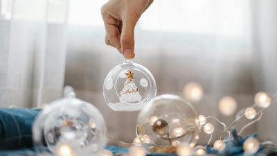 Hand holding a festive bauble amidst twinkling fairy lights