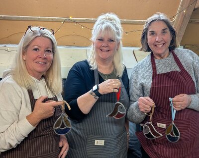 Three smiling ladies showing off their handmade glass bird decorations.