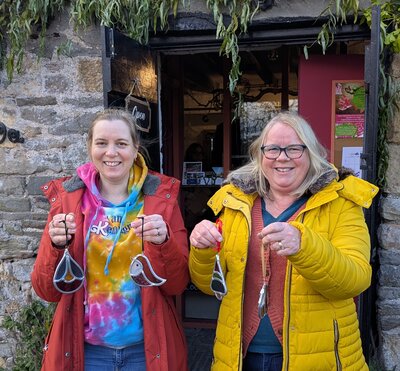 Two happy women showcasing handmade glass art outside a cosy workshop.