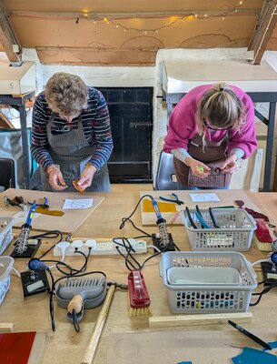 Two people in a cosy workshop, joyfully crafting stained glass art.