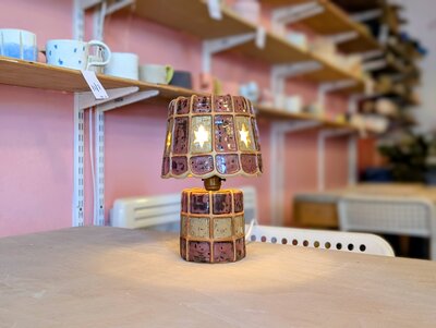 Ceramic lamp with glowing star cutouts on a cosy workshop table.