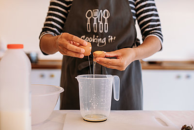 Guest wearing Cooking It apron cracks an egg into a measuring jug